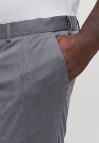 Grå, teksturerte bukser med et glatt stoff, som har en midje, sidelommer og en slim fit-design.