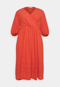 Robe rouge en tissu léger, de style enveloppant. Elle possède des manches bouffantes 3/4 et des détails froncés à la taille et à l'ourlet.
