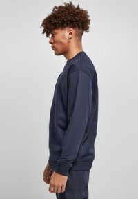 Sudadera azul marino confeccionada en un tejido suave, con escote tipo crew, puños acanalados y un corte relajado, vista de lado.