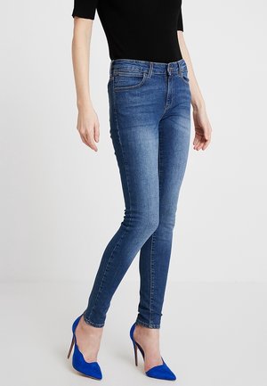 Wąskie niebieskie dżinsy z denimu o średnim stanie, z przednimi kieszeniami i subtelnym spraniem. Łączone z jasnoniebieskimi szpilkami i dopasowaną czarną bluzką.