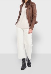 Brun läderbikerjacka, krämfärgad tröja med ribbad nederkant, vita vida byxor och svarta kraftiga stövlar. Släta texturer och lagerdesign.