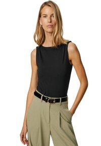 Svart ärmlös topp med rund halsringning, kombinerad med högmidjade beige byxor och ett svart bälte med ett guldspänne.