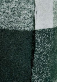 Grön och grå ulltyg med varierande texturer, som har en blandning av enfärgade och mönstrade lappar, vilket framhäver en mjuk, fluffig look.