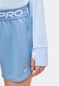 Gros plan d'une personne portant un short de sport Nike bleu clair et un haut à manches longues assorti avec des trous pour les pouces aux manches.
