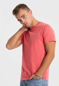 Koralfarvet bomulds t-shirt med korteærmer og rund halsudskæring. Glat tekstur, afslappet pasform, parret med lyseblå jeans.