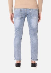 Jeans di denim azzurro chiaro con una vestibilità slim, dotati di cinque tasche, leggermente sbiaditi e con i risvolti. Indossati con sneakers nere.