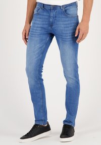Slim-fit modri kavbojki iz denima z nežnim gubanjem, kontrastnim šivom, petimi žepi in standardnim gumbom za zapiranje.
