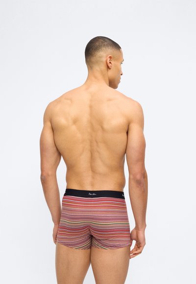 Homme aux cheveux courts vu de dos, portant un boxer rayé multicolore avec une ceinture noire.