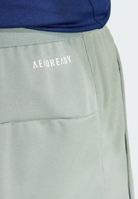 Hellgrüne Shorts bestehen aus einem strukturierten Stoff, haben einen elastischen Bund und ein sichtbares weißes "AEROREADY"-Logo an der Seite.