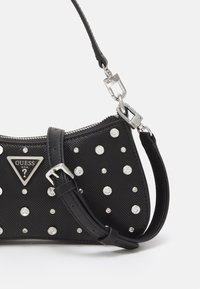 Czarna torebka z teksturowanej tkaniny, ozdobiona akcentami w postaci kryształków, z trójkątnym metalowym logo oraz regulowanym paskiem z srebrnym zapięciem.