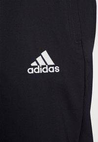 Svarta träningsbyxor i lättviktsmaterial, med en vit broderad Adidas-logotyp på vänster ben och en slät yta.
