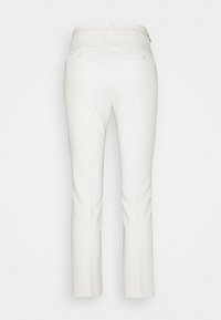 Pantalon blanc sur mesure vu de dos, avec poches arrière boutonnées et coupe droite.