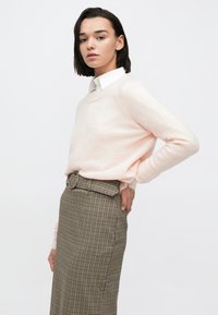 Ανοιχτό ροζ πουλόβερ με λαιμόκοψη, συνδυασμένο με καρό φούστα ψηλόμεση που διαθέτει ζώνη. Ομαλή υφή, απαλό ύφασμα.