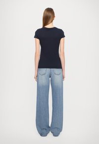 T-shirt in cotone blu navy a maniche corte e jeans in denim blu chiaro a gamba larga con wash sbiadito, dotati di tasche posteriori e vestibilità comoda.