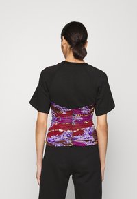 Svart kortärmad topp med en åtsittande, flerfärgad mönstrad rynkad rygg, med lila, röd och guld accentuerade detaljer. Slät texture.