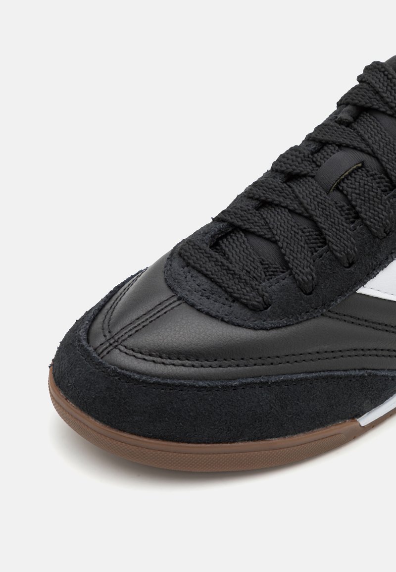 Scarpa sportiva nera con tomaia in suede testurizzato e pelle liscia. Presenta una suola in gomma marrone e lacci neri con dettagli bianchi.