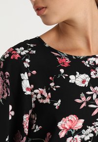 Blusa negra con estampado floral que presenta un cuello redondeado, con flores en tonos rosa y blanco de diferentes tamaños y una textura de tela suave y ligera.
