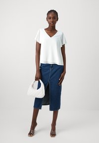 White short-sleeve blouse with a V-neck, paired with a denim skirt that features a front slit, held with a textured white handbag.