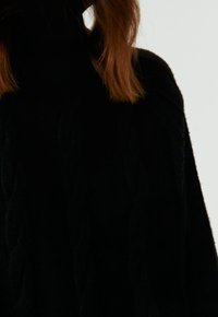 Pull en maille noir avec un col montant et un motif en câble texturé. Le tissu semble doux et épais, offrant chaleur et confort.
