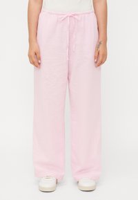 Pantaloni larghi in lino rosa chiaro con vita elastica e cordoncino. Il tessuto ha una finitura leggermente strutturata. Indossati con sneaker bianche.