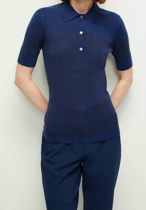 Osoba ubrana w dopasowaną granatową koszulkę polo z krótkim rękawem, z brązowymi poziomymi paskami i złotymi guzikami, w zestawie z ciemnoniebieskimi spodniami.