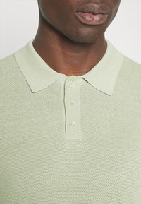 Jasnozielony dzianinowy polo z klasycznym kołnierzykiem, wykonany z teksturowanej tkaniny, z trzema guzikami przy dekolcie.