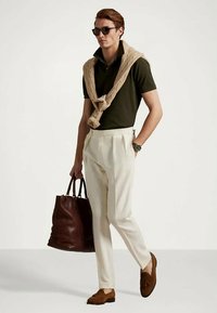 Tamsiai žalia polo marškinėliai, kreminės spalvos plisėti kelnės, ruda odinė rankinė ir smėlio spalvos loafers batai. Megztinis užmestas ant kaklo; dėvimi saulės akiniai.