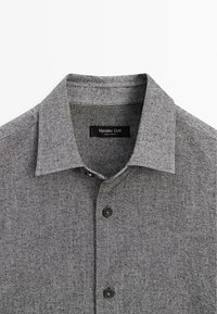 Camicia grigia con colletto, realizzata in tessuto testurizzato. Presenta bottoni neri e un'etichetta con il marchio "Massimo Dutti".
