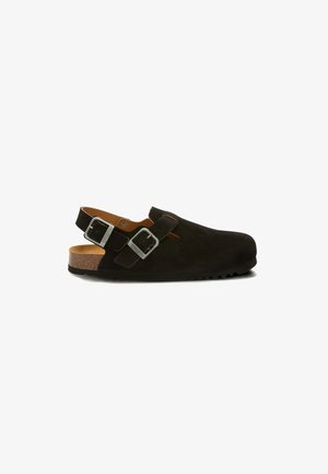 Zwarte suède sandalen met gesloten tenen, verstelbare zilveren gespen en een kurk voetbed, op een witte achtergrond, zijaanzicht.