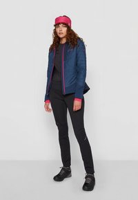 Μπλε μονωμένο μπουφάν με ροζ λεπτομέρειες, συνδυασμένο με μαύρο τοπ και παντελόνια. Μια ροζ κορδέλα στα μαλλιά συμπληρώνει τα αθλητικά παπούτσια.