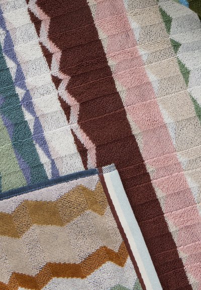 Gros plan sur des tapis texturés avec des motifs en zigzag dans des couleurs comme marron, rose, vert, violet et moutarde, disposés en chevauchement.