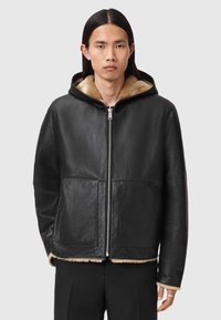 Schwarze Lederjacke mit Kapuze und weichem, beigefarbenem Kunstpelzfutter, mit Reißverschluss vorne und zwei großen, vorderen Taschen. Gleiche Textur und lockere Passform.