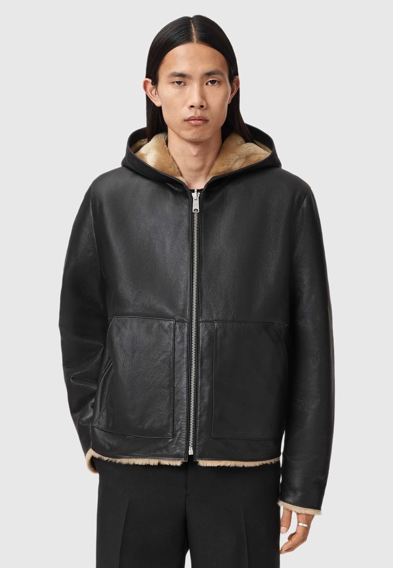 Schwarze Lederjacke mit Kapuze und weichem, beigefarbenem Kunstpelzfutter, mit Reißverschluss vorne und zwei großen, vorderen Taschen. Gleiche Textur und lockere Passform.