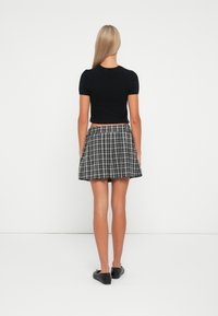 Maglietta nera corta abbinata a una gonna svasata a tre quarti in tartan bianco e nero, completata da scarpe nere basse.
