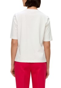 White cotton t-shirt with short sleeves, round neckline, and a relaxed fit, paired with pink tailored pants. Textured fabric, simple design.