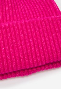 Bonnet tricoté rose vif avec une texture côtelée et un ourlet replié. Le matériau semble doux et chaud, adapté aux temps froids.