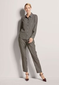 Schwarz-weiß gemusterte Bluse mit langen Ärmeln, Knopfverschluss, kombiniert mit passenden gemusterten schmalen Hosen und spitzen burgunderroten Absätzen.
