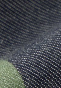 Gros plan sur un tissu texturé bleu et vert avec des fils tissés visibles et des variations subtiles d'ombrage.