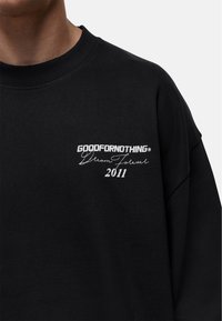 Felpa nera con testo ricamato "GOODFORNOTHING," "Dream Forever," e "2011" in bianco, design a girocollo e vestibilità comoda.