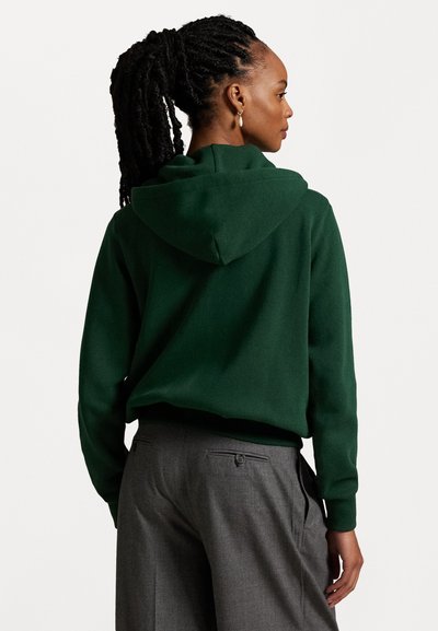 Mørkeblå hoodie med en afslappet pasform, der har hætte og ribbede manchetter, parret med grå skræddersyede bukser. Glat struktur, minimalistisk design.