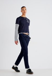 Chemise navy à manches courtes avec manches longues rayées, détail de numéro gris, associée à un pantalon navy et des chaussures noires, dotée d'une ceinture plate.
