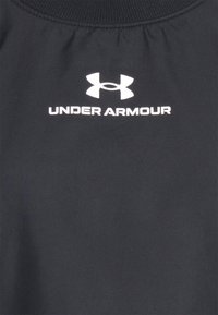 Černý sportovní top s jemnou texturou, s žebrovaným zpevněním kolem krku a bílým logem "Under Armour" nad stylizovaným logem.