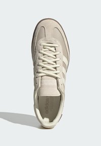 Krämlfärgade sneakers med en blandning av mocka och mesh-material, med ett texturerat snörningsparti och tre ikoniska ränder på sidan.