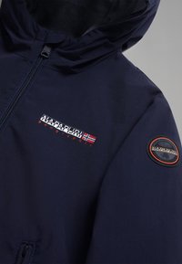 Marinblå jacka med huva, med en frontdragkedja, logotypapplikation på ärmen och kontrasterande orange text på bröstet. Slät textur.