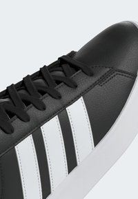 Baskets noires avec des bandes blanches, des lacets noirs, une tige en cuir texturé et une semelle blanche en caoutchouc, vues de côté et de dessus.