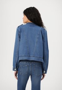 Denim jacket in medium blue with a cropped cut, shoulder epaulets, and a slightly distressed hem. Features a smooth texture and classic stitching.