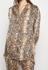 Brun och svart ormtrycksskjorta med långa ärmar, krage och knappdetalj fram. Slät, silkig textur.