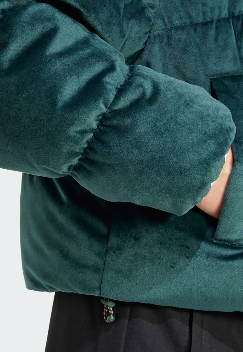 Tannenzapfenfarbene Samt-Pufferjacke mit strukturiertem Finish, ausgestattet mit einem gekrempelten Ärmel und einer seitlichen Tasche, die am Saum mit einem Toggle geschlossen wird.