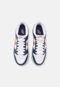 Nike sportbačiai su balta odine viršutine dalimi, tamsiai mėlynais akcentais, perforuota pirštų zona ir auksiniu swoosh. Yra balti raišteliai ir paminkštinta apykaklė.