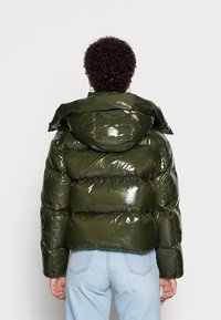 Skinnende, pufferjakke i mørkeoliven med hætte, der har en boksformet silhuet og synlige syninger.